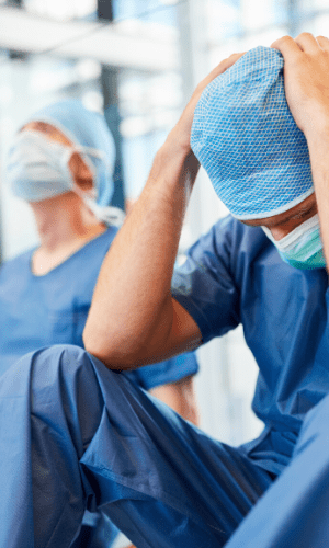 picture of a doctor in blue scrubs sitting down and holding his head