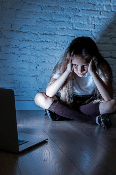 little girl crying as she's sitting in a dim room looking at her computer